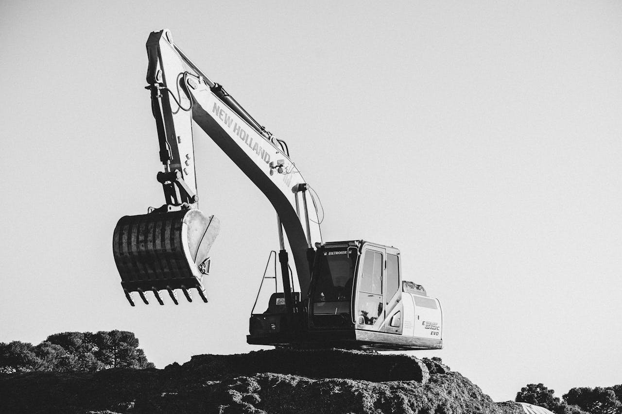 Home Black and white image of an excavator at a construction site under a clear sky.